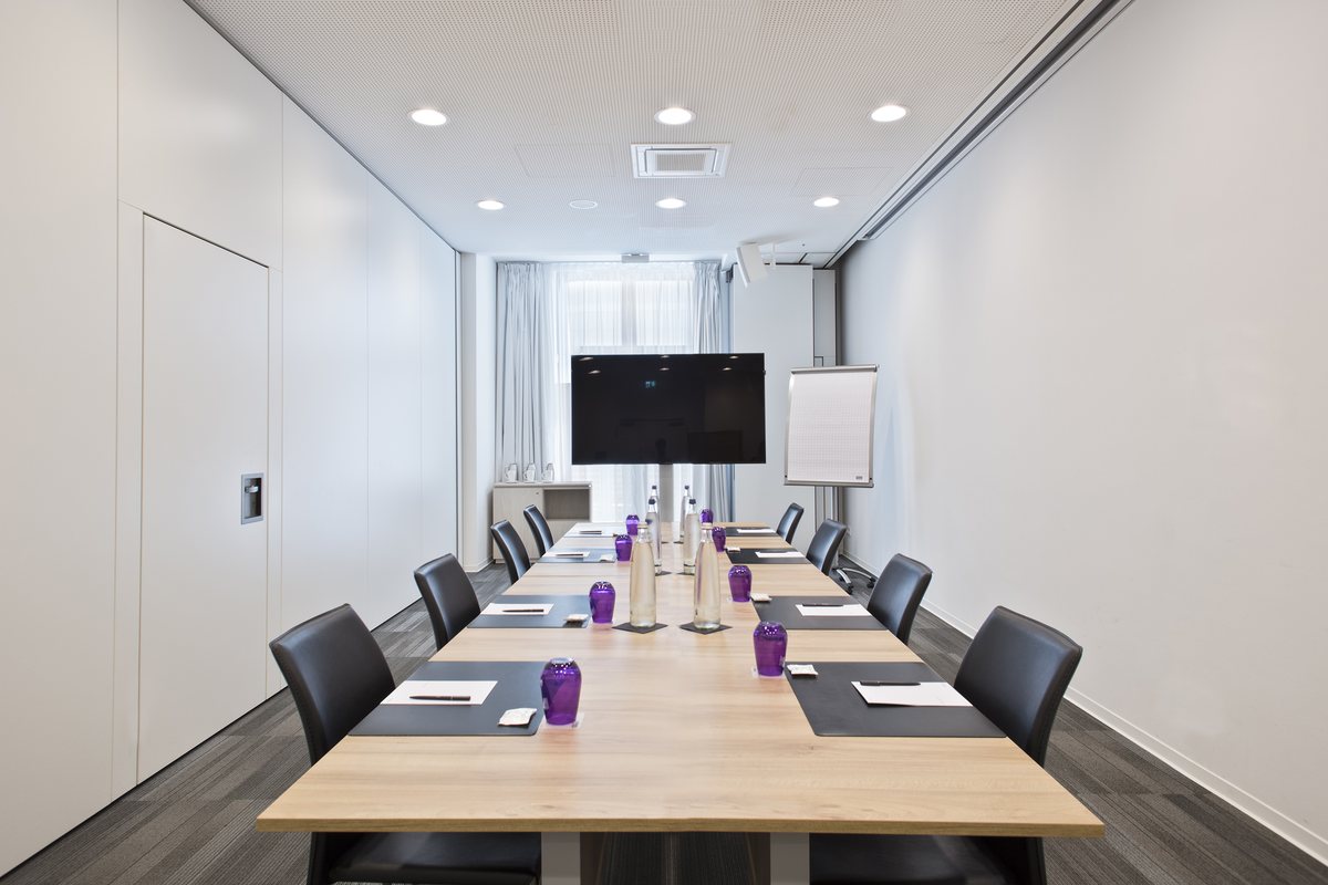 Bright meeting room with a long wooden table, screen and flipchart, prepared for a workshop